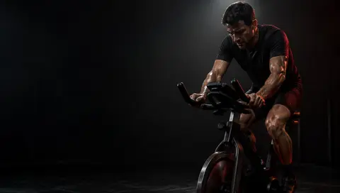 Soustředěný jezdec na indoor cycling kole v bodovém a červeném kontrasvětle